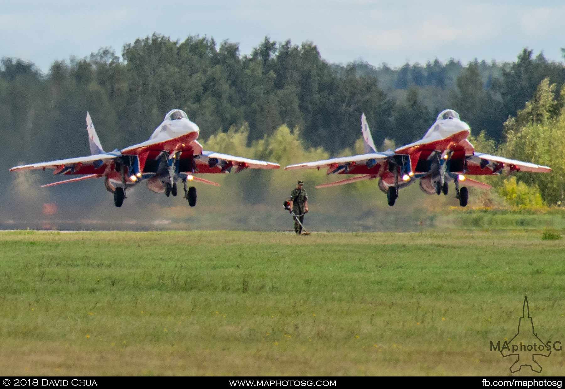 33. A soldier on grass cutting duty as a pair of MiG-29s of the Swifts Aerobatic Team takes off