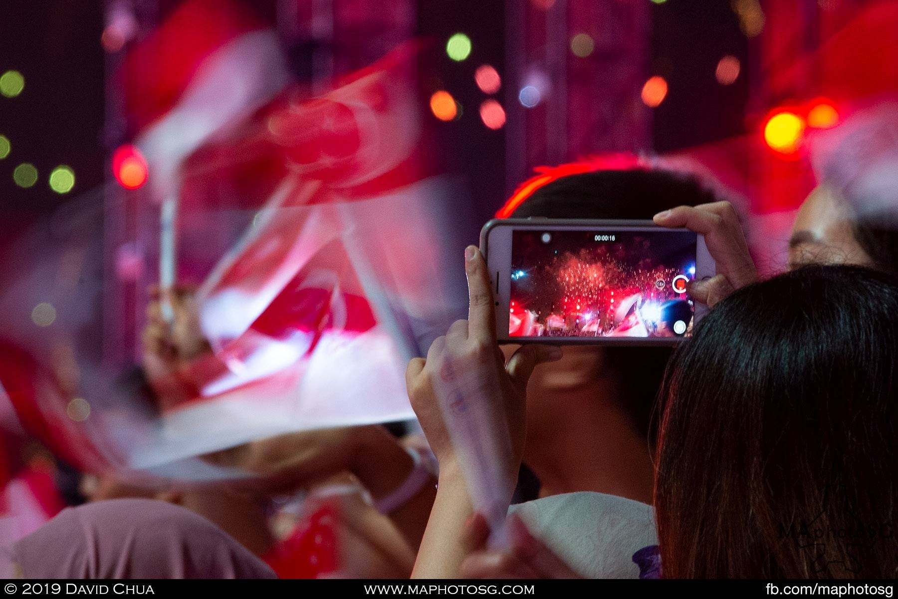 A mobile phone records the finale fireworks as the crowd waves the flag