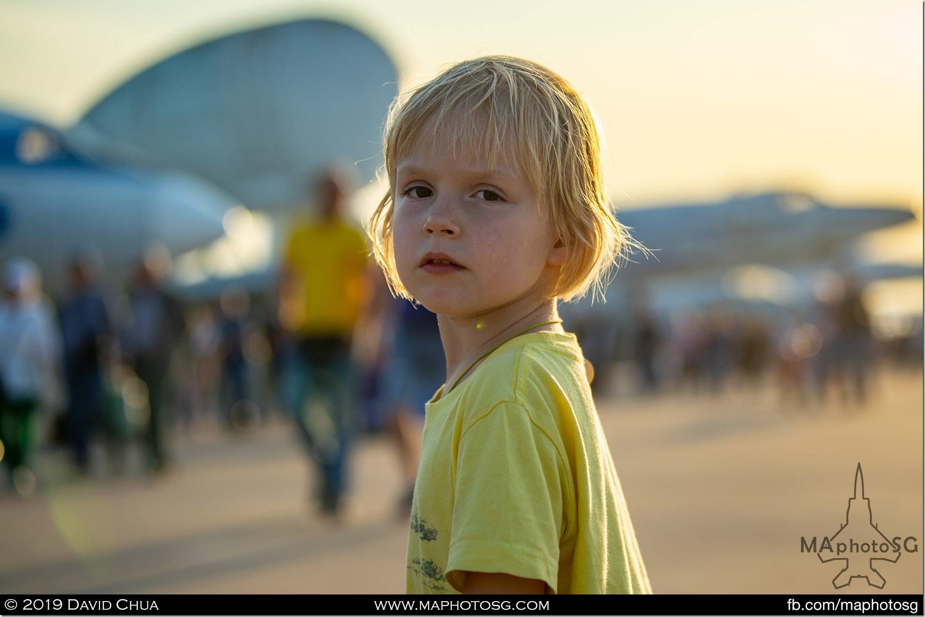 A young boy looks bad at the camera as he wonders amongst aeroplanes